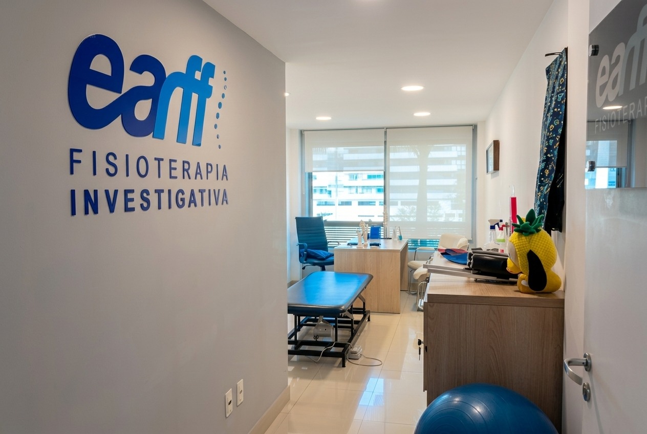 Corredor de entrada da unidade EARFF Freguesia com parede cinza exibindo o logo azul EARFF Fisioterapia Investigativa, ao fundo consultório clínico com maca de fisioterapia azul, mesa de madeira clara com materiais de atendimento, janelas com persianas e vista para prédios, piso porcelanato claro, boneco de pelúcia amarelo sobre o móvel, iluminação natural suave, fotografia realista